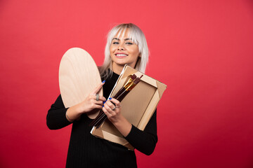 Young artist woman holding art supplies on a red background