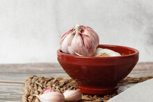 Garlic On Wooden Table In Bowl On Raffia Tablecloth And Kitchen Towel, Close Up View