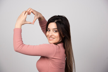 Smiling girl in pink t-shirt showing heart with two hands