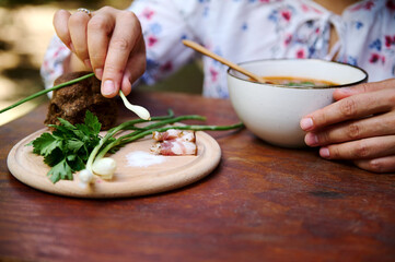 Wall Mural - Close-up hands of a woman holding green onions while eating delicious traditional Ukrainian red beet soup - Borscht