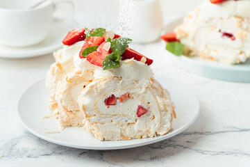 Wall Mural - Meringue roll sprinkled with powdered sugar decorated with strawberries sliced and served in the white plate on the white background. Macro shot