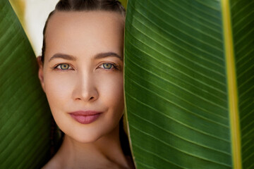 Organic cosmetic concept. Green beauty portrait. Beautiful young woman posing against and behind fresh green tropical banana leaves.