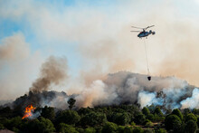 Helicóptero A Transportar água Para Apagar Um Incêndio Florestal Que Arde Num Pinheiral Deixando Uma Grande Nuvem De Fumo Branco E Negro