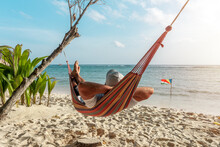 Tourist Relaxing In A Hammock On A Tropical Beach Overlooking The Indian Ocean. La Digue Island, Seychelles