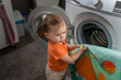 One girl small caucasian toddler child daughter standing at the washing machine in the toilet opening or closing the door examine and learn early development and growing up mischief concept copy space