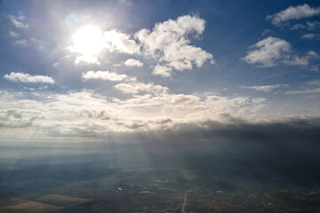 Aerial view from high altitude of distant city covered with puffy cumulus clouds forming before rainstorm in evening. Airplane point of view of cloudy landscape