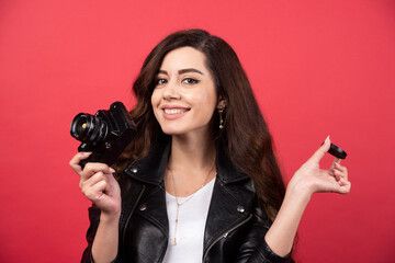 Poster - Beautiful woman photographer holding photo camera on a red background