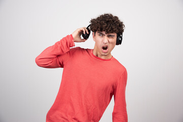 Wall Mural - Curly young man with headphones listening to song with loud volume