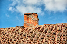 Red Brick Chimney Designed On The Roof Of Residential House Or Building Outside Against A Cloudy Sky Background With Copyspace. Air Vent Construction For The Release Of Smoke And Heat From Fireplace