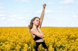 © Julia Jones - a girl in a black top and black trousers stands with her hand raised up in a yellow rapeseed field in spring