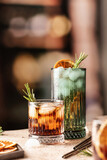 Cocktails on the bar. Whiskey-cola, cuba libre iced cocktails with rosemary and dried orange slices with metal straws behind. Text space