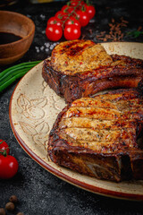 Wall Mural - Grilled pork loin, pork steak on the bone on a dark stone table with vegetables, cream and tomato sauce. Served on a clay plate. Fast food restaurant, delivery service.