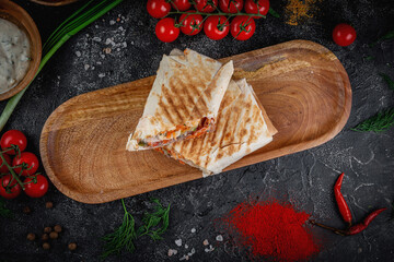 Sticker - Shawarma with vegetables on a wooden board with pita sauce on a dark stone table decorated with cherry tomatoes. Fast food restaurant, delivery service.