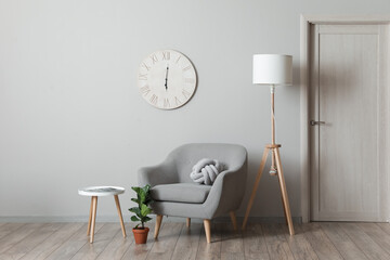 Comfortable armchair with lamp, table and houseplant near light wall in room