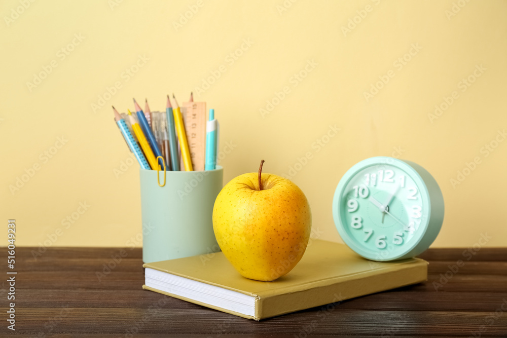 School stationery with apple and alarm clock on table against color background