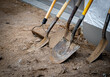 Dirty used shovels and a rake lean against a wall during a work break at a new home construction job site.