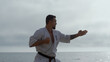 © stockbusters - Man making karate kicks on seacoast close up. Athlete training fighting skills.