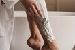 © Damir Khabirov - Cropped shot of woman hand depilating shins in shaving foam with razor over bathtub on background