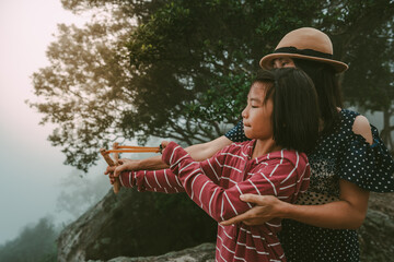 Wall Mural - Children and mother holding slingshot for shooting seed of plants to forest on foggy and sky morning background 