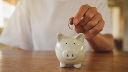 Wall Mural - Closeup image of a woman putting coin into piggy bank for saving money concept