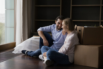 Wall Mural - Joyful happy young couple taking break at paper boxes, enjoying leisure after moving, relocation into new home, smiling, laughing, discussing shipping, transportation service. Apartment buying concept