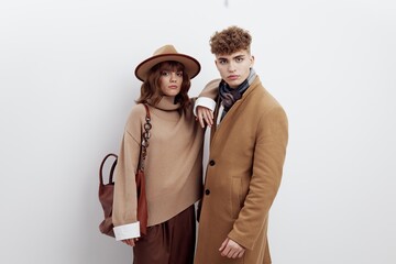 a cute couple, a man and a woman are standing on a white background in autumn clothes and a woman is leaning on a man with her hand on his shoulder, holding a large brown bag