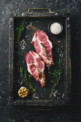 Wall Mural - Fresh pork. Two pork steaks. Top view. On a black stone background.