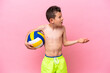Little caucasian boy playing volleyball isolated on pink background with surprise facial expression