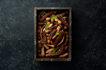 Wall Mural - Exotic tamarind fruits in a box. Top view. On a stone background.