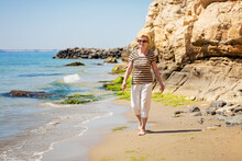 Elderly Attractive Woman Walking Along The Seashore And Enjoying The Moment