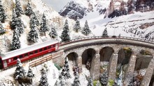 Red Model Train In Miniature Passing On Viaduct. Model Railway, Alps Moutain Ambientation.