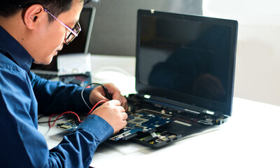 young man who is a computer technician A laptop motherboard repairman is using an IC meter to look for defects on the motherboard to repair on his desk. Board repair with modern technology