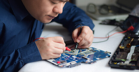 young man who is a computer technician A laptop motherboard repairman is using an IC meter to look for defects on the motherboard to repair on his desk. Board repair with modern technology