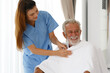 © atitaph - A female nurse uses a blanket to a senior Caucasian man sitting in a wheelchair