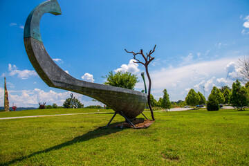 a grey boat shaped sculpture surrounded b a gorgeous summer landscape with lush green trees and grass with blue sky and clouds at Sculpture Fields at Montague Park in Chattanooga Tennessee USA