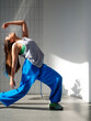© Ulia Koltyrina - Modern dance, stylish young brunette in baggy blue pants dancing in jazz-funk style. Stylish and youthful. The dance hall is illuminated by sunlight, bright colors