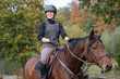 junge Frau lacht bei Ausritt auf braunem Pferd im Herbst