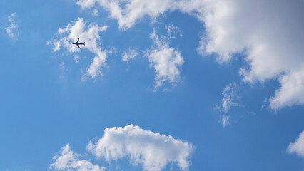 Wall Mural - The passenger airplane is flying far away in the blue sky and white clouds. Aircraft in the air. Light background or backdrop about international passenger air transportation