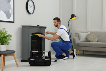 Professional technician with measuring tape installing electric fireplace in room