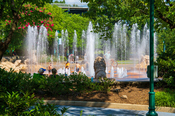 Wall Mural - children playing in a water fountain surrounded by a gorgeous summer landscape with pink trees and lush green trees, grass and plants at Coolidge park in Chattanooga Tennessee USA