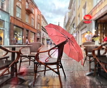   Pink Umbrella On Chair   In Street Restaurant Rainy City People Walk With Umbrellas On Wooden Table Glass With Candlr Light Rain Drops In Medieval Street Houses In Tallinn Old Town Urban Lifestyle 