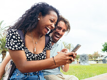 Happy Diverse Smiling Heterosexual Young Couple Looking At Mobile Phone And Smiling In A City. Social Media And Vacation Concept