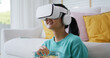 © ChayTee - Asia people teen girl enjoy play AR media online sitting laugh humor joy at cozy sofa relax eat food wear eye glasses tv display fun video game in cyber app. Overjoy smile in VR augmented film.