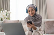 © Natee Meepian - Muslim female using mobile phone and laptop computer sitting on office room at home