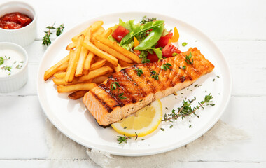 Wall Mural - Salmon steak with vegetables and fries on light background.