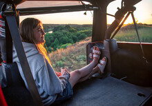 A Young Woman Enjoys The Sunset While Sitting In The Trunk Of An SUV.