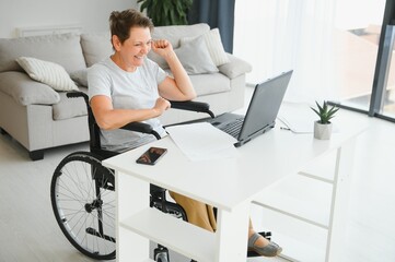 Poster - Middle age woman using laptop sitting on wheelchair at home