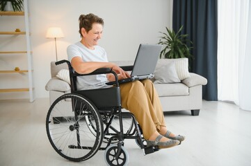 Poster - Middle age grey-haired disabled woman having video call sitting on wheelchair at home.