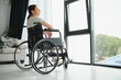 © Serhii - woman looking away while sitting in wheelchair at home