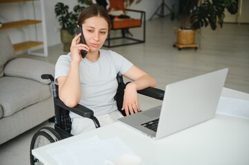 woman in a wheelchair works on the laptop PC in the home office with an assistance dog as a companion